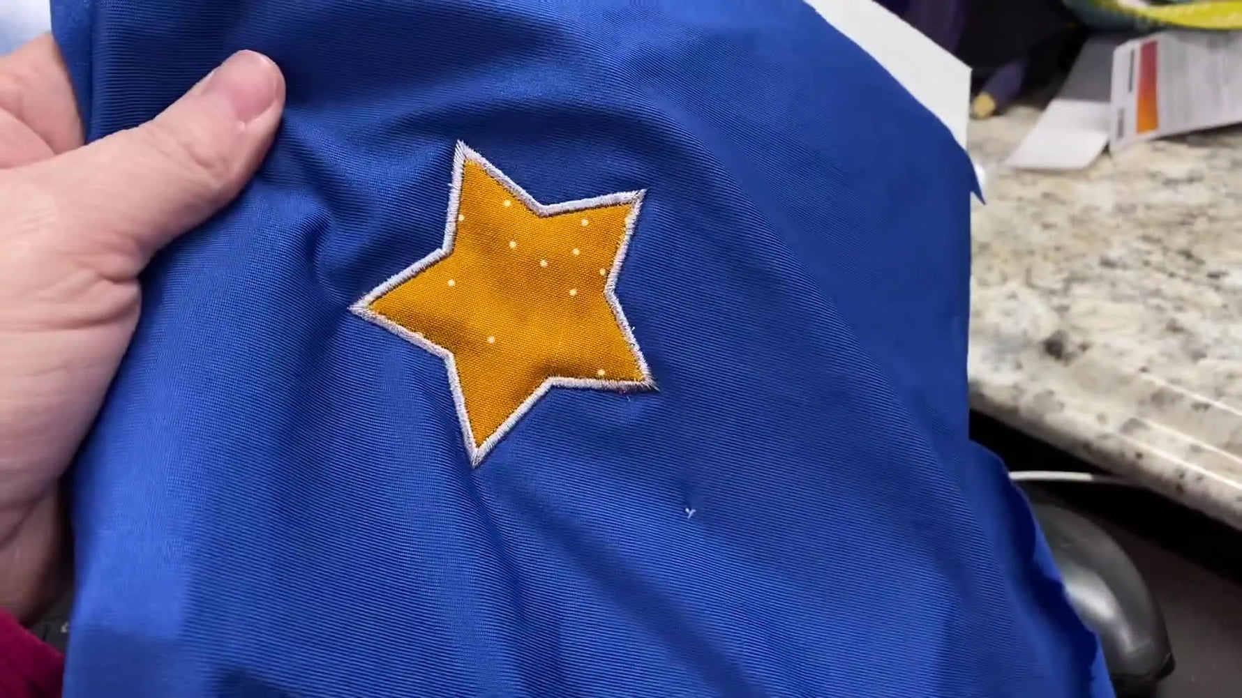 A close-up of a finished orange star appliqué with satin stitching on a blue sweatshirt, showing clean edges and accurate placement.