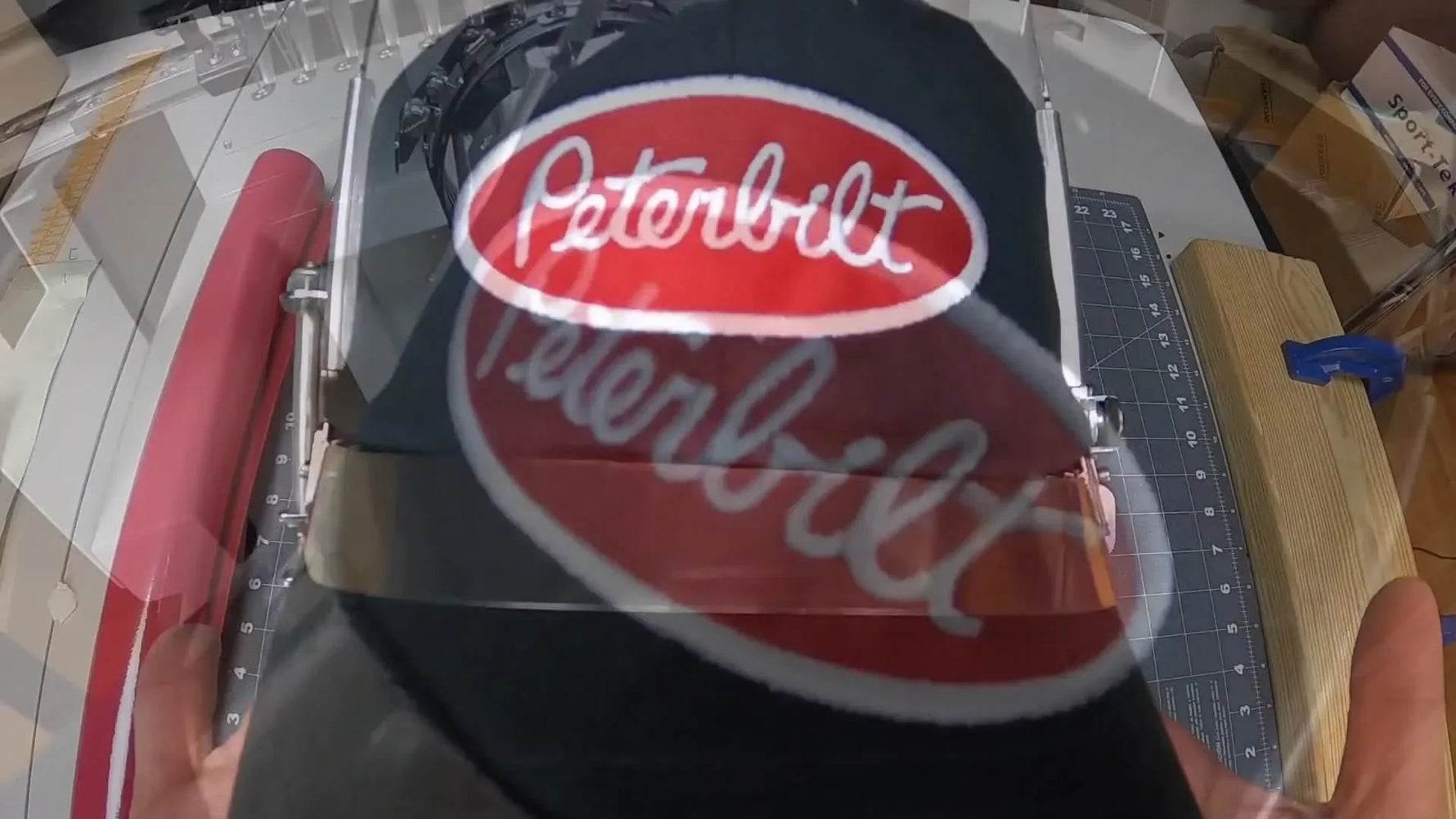A finished Peterbilt-style appliqué logo hat sits in the magnetic hoop, showing a crisp satin border that fully covers the trimmed twill edge.
