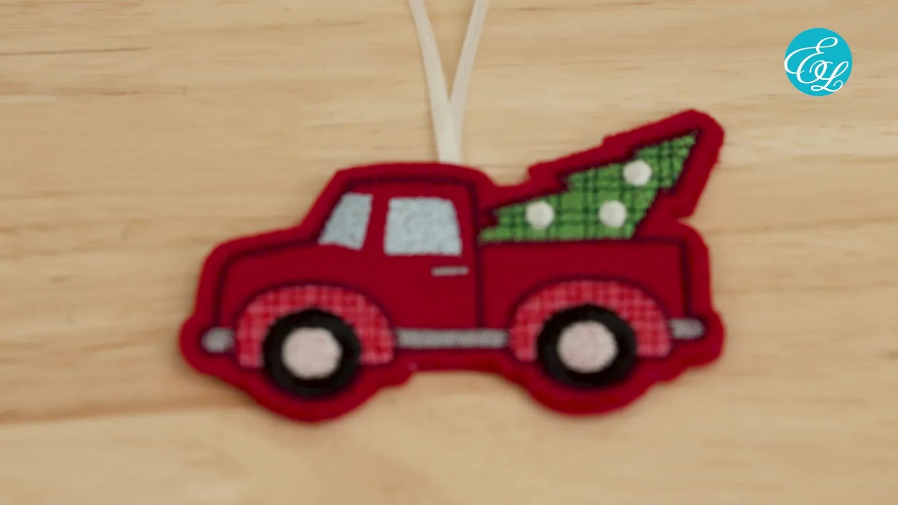 A finished red truck in-the-hoop ornament hangs neatly with crisp edges, clean stitching, and a ribbon loop ready for gifting.