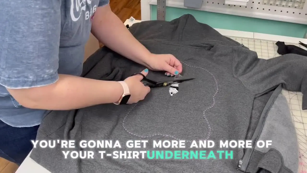 Scissors cutting away the grey hoodie fabric to reveal the colorful Stormtrooper applique underneath, demonstrating the reverse applique technique.