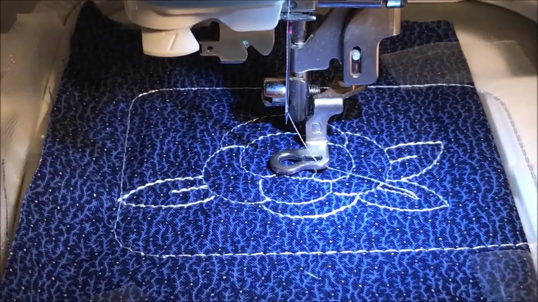 A close-up of the Brother SE425 embroidering a small white rose motif on blue fabric inside a 4x4 hoop.