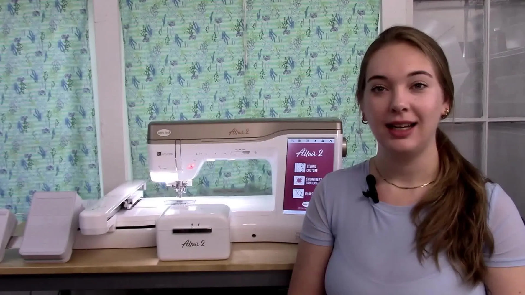 The host stands beside a Baby Lock Altair 2 with the embroidery unit attached, setting up a walkthrough of the machine’s new features.
