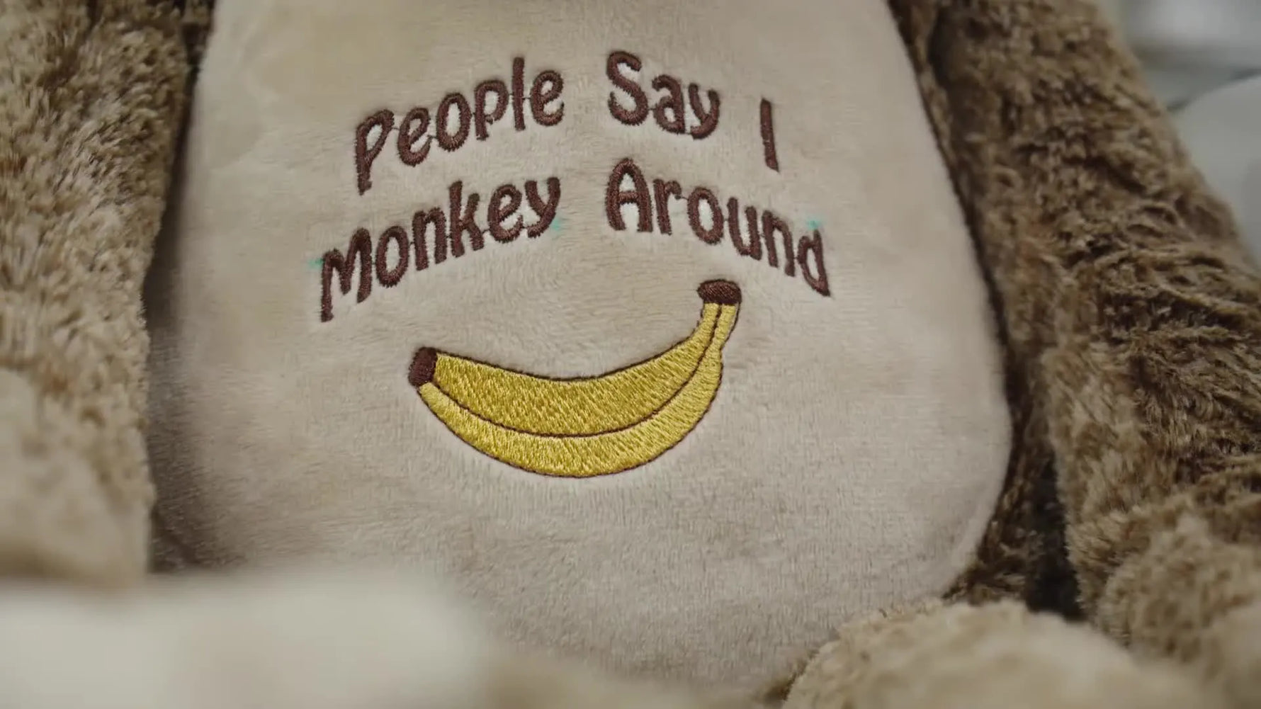 A finished plush monkey is held up to the camera, showing clean, readable embroidery on the belly with the toy fully re-stuffed.