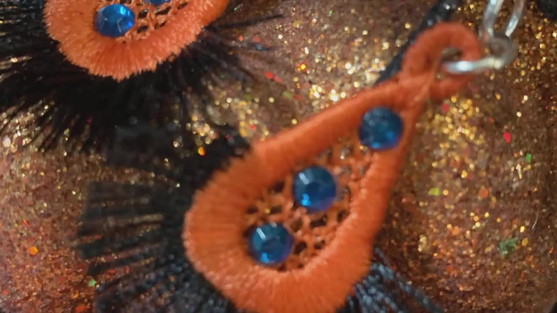 Finished Halloween-color freestanding lace fringe earrings with rhinestone bling displayed on a glittery pumpkin background.