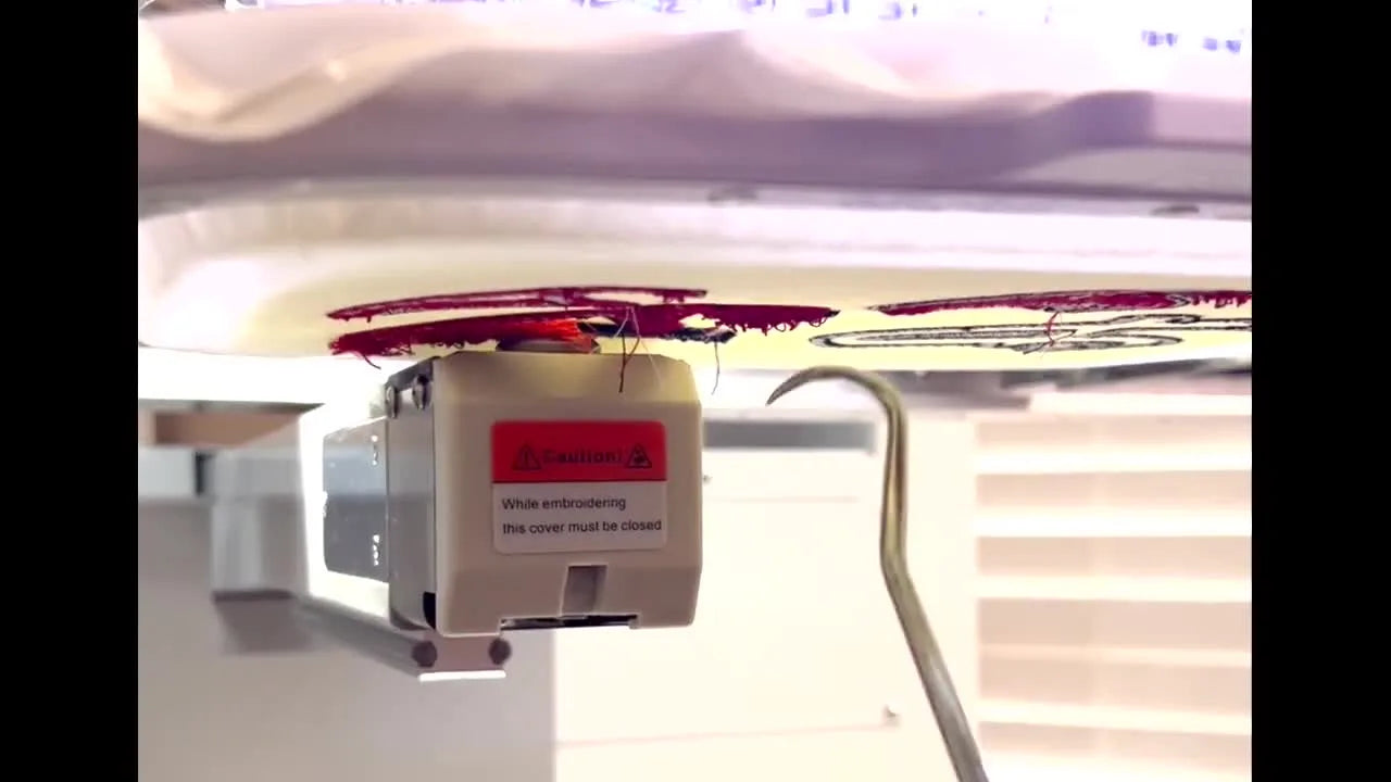 Close-up of a long hook tool pulling a red thread bird’s nest forward while a stitch releaser knife is positioned to cut it free.