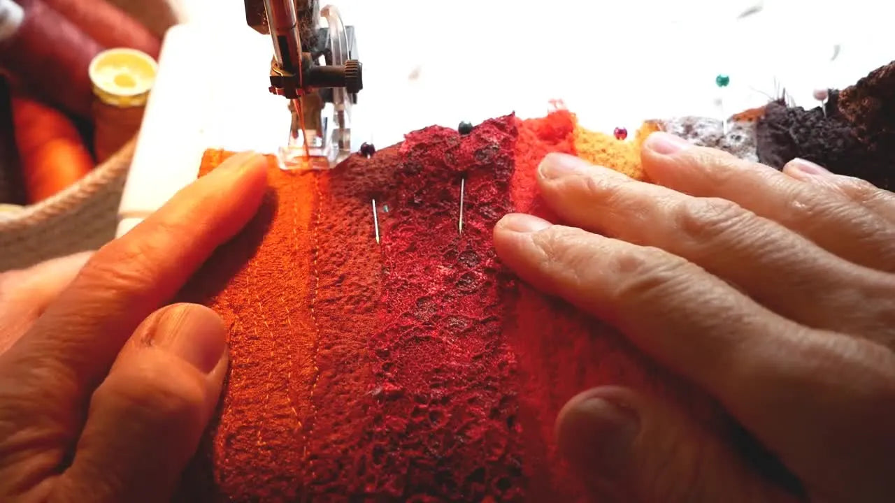 Close-up of a sewing machine needle over red fabric, with hands guiding the fabric for free machine embroidery.