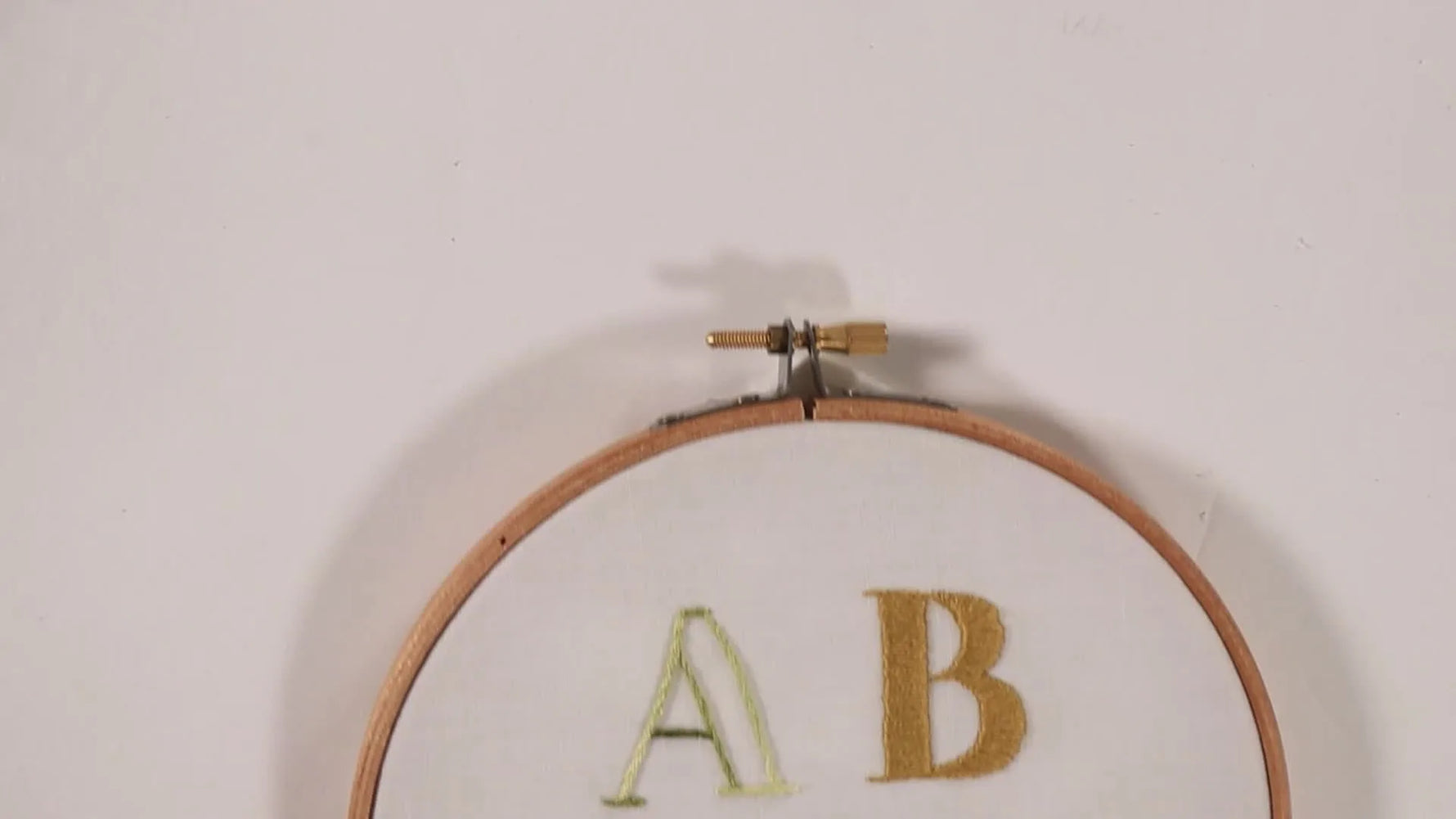 Top-down view of an oval embroidery hoop displaying five block letters (A-E) stitched with different embroidery styles.