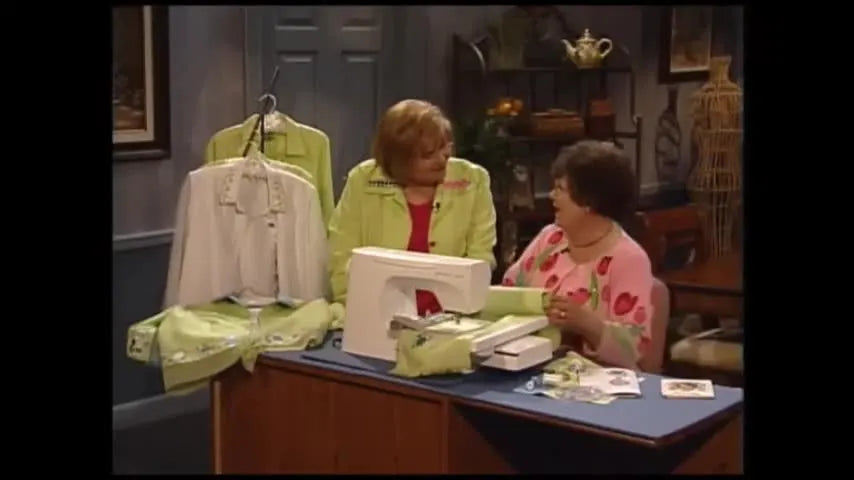 A garment is rolled tightly onto a long cardboard tube beside an embroidery hoop to keep bulk controlled while stitching a continuous border.