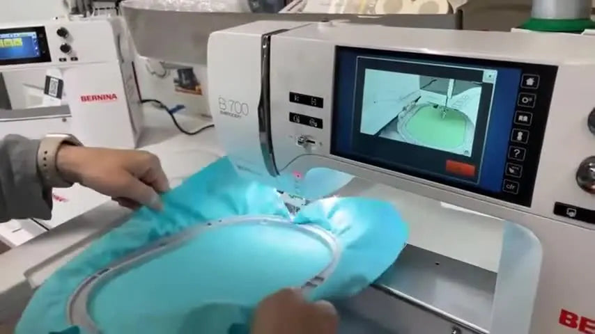 Margaret slides the hooped teal fabric onto the Bernina B700 embroidery module arm, showing the click-in attachment mechanism.