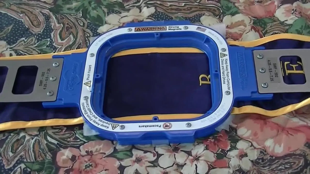 A magnetic hoop clamped sideways across a satin graduation sash, showing the safer orientation that keeps long tails away from the pantograph.