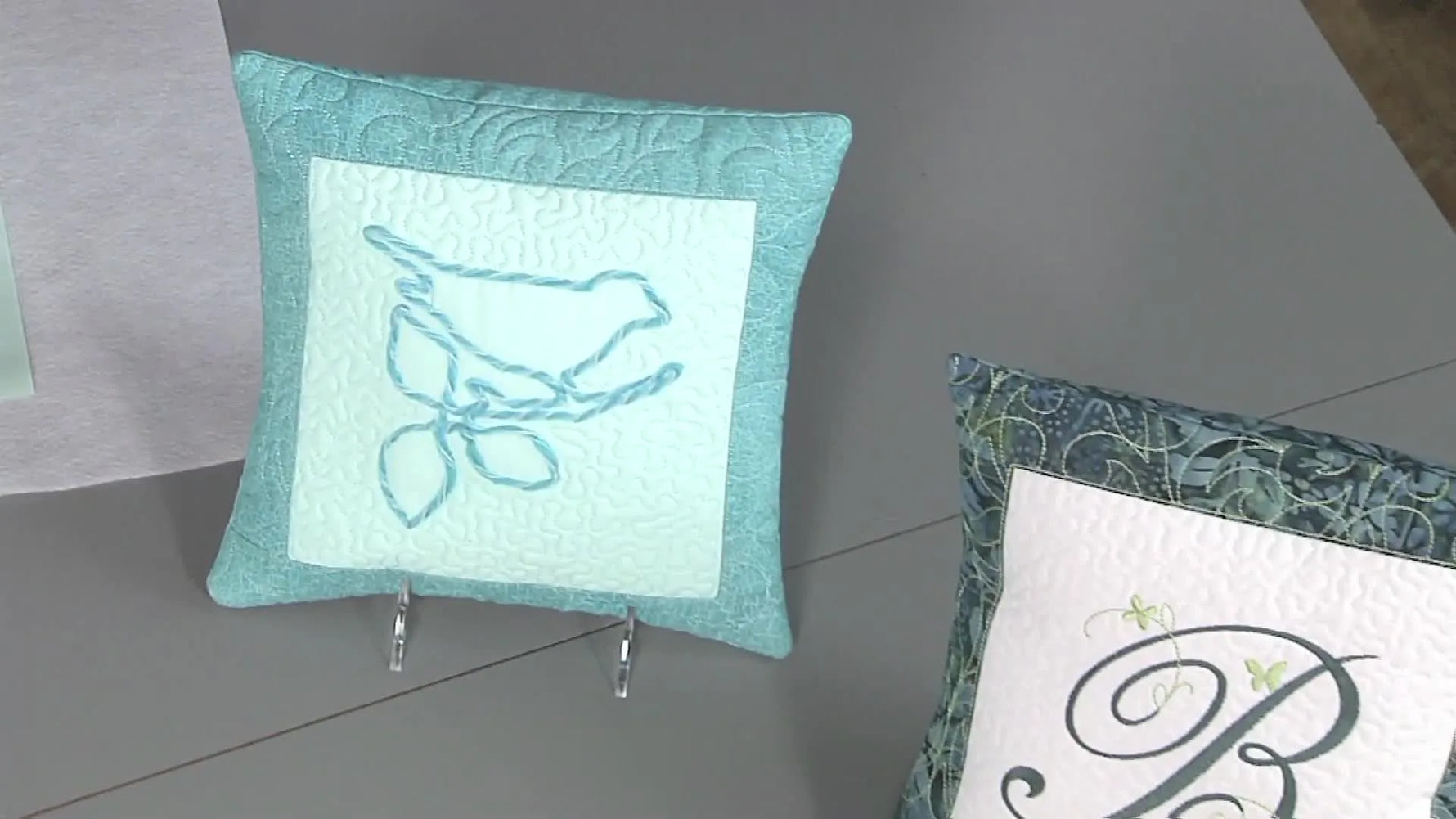 A close-up of the finished teal pillow featuring a textured couched-yarn bird on the front.