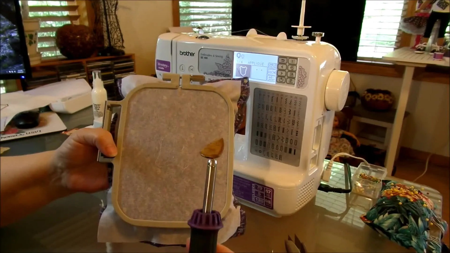A mini craft iron heat-sets a glued appliqué patch inside a hooped fabric on a Brother SE-400 setup.