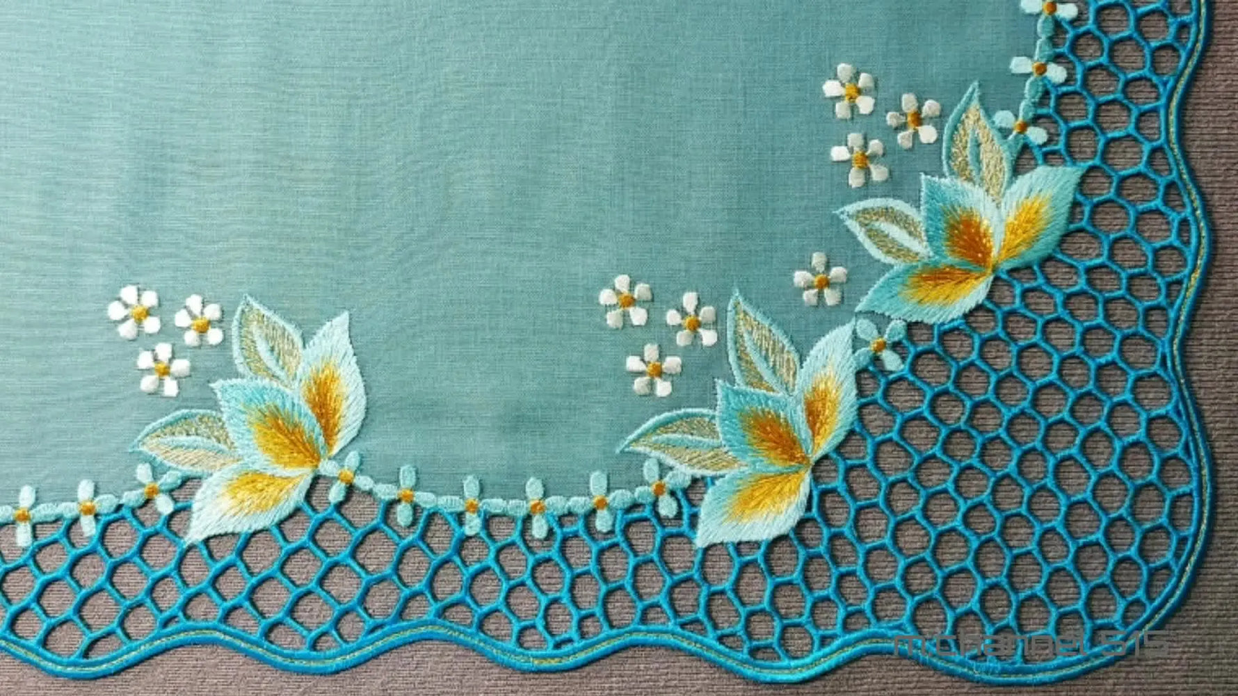 Finished cutwork embroidery design on light teal fabric, featuring a honeycomb border and floral motifs.