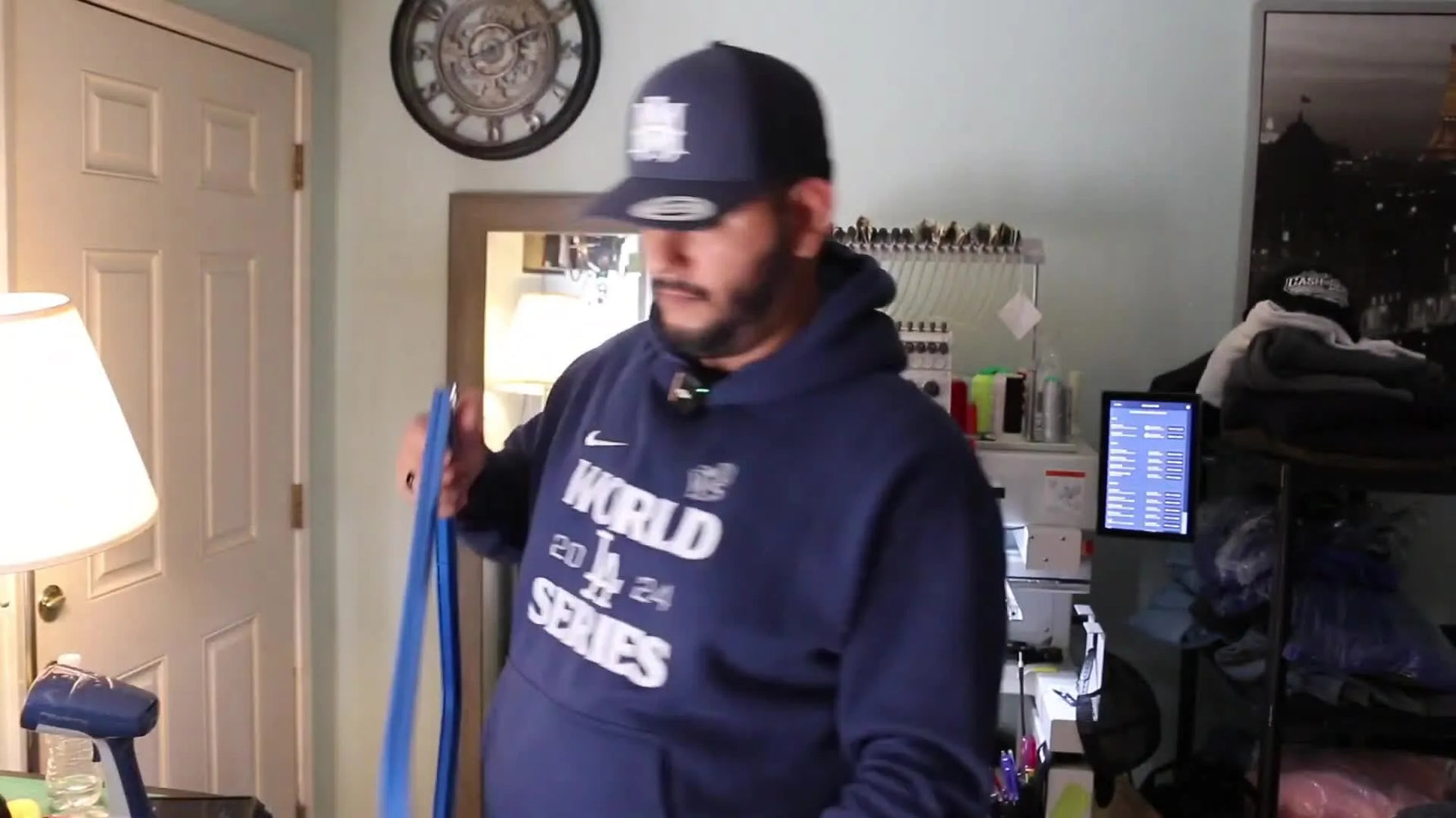 The host holds the fully unpacked blue Sew Talent magnetic hoop in front of a Ricoma Marquee 2001, ready for a strength and workflow comparison.