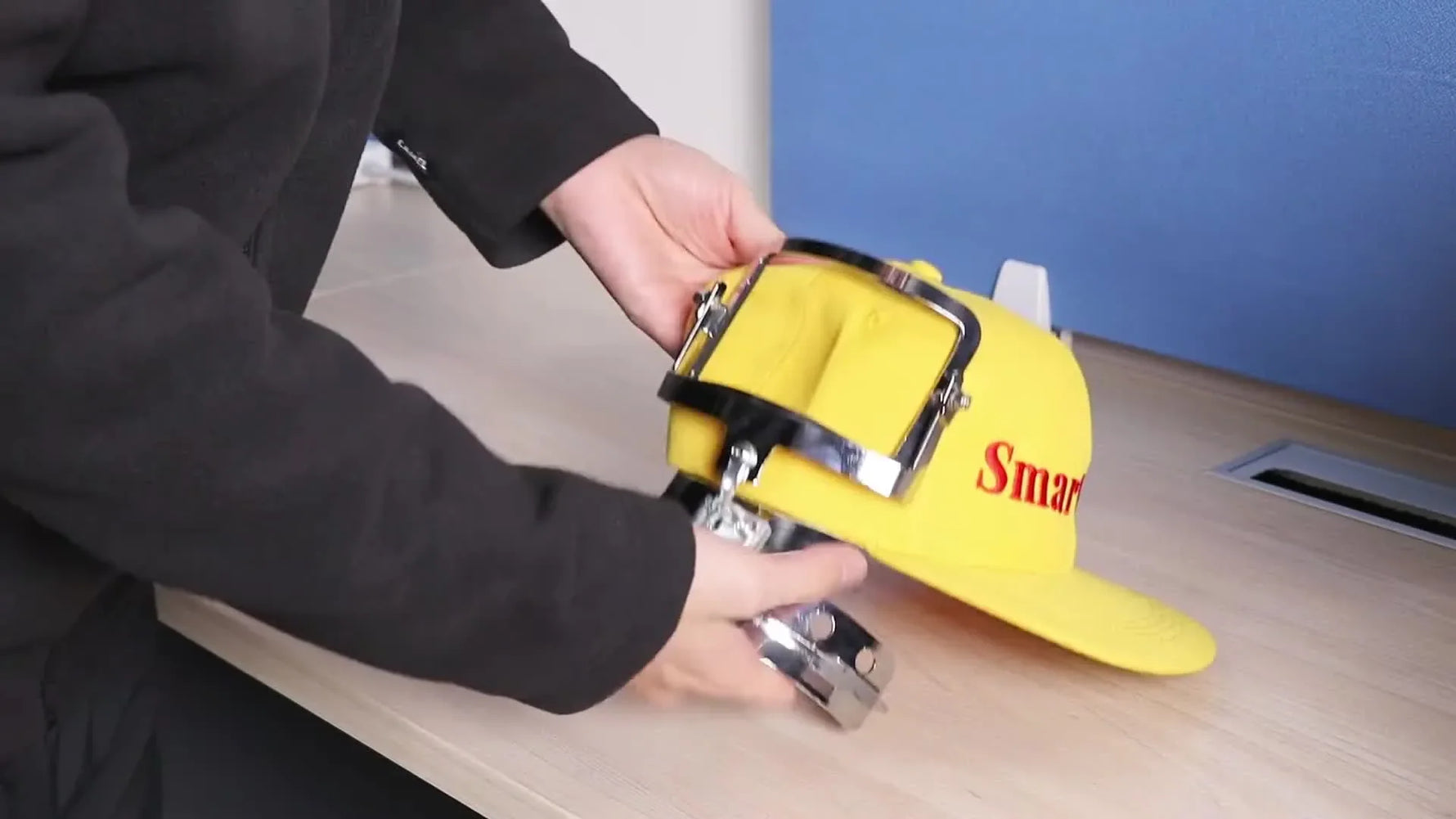A close-up of hands pressing the top magnetic frame down to clamp a structured yellow cap securely in a curved pocket hoop.