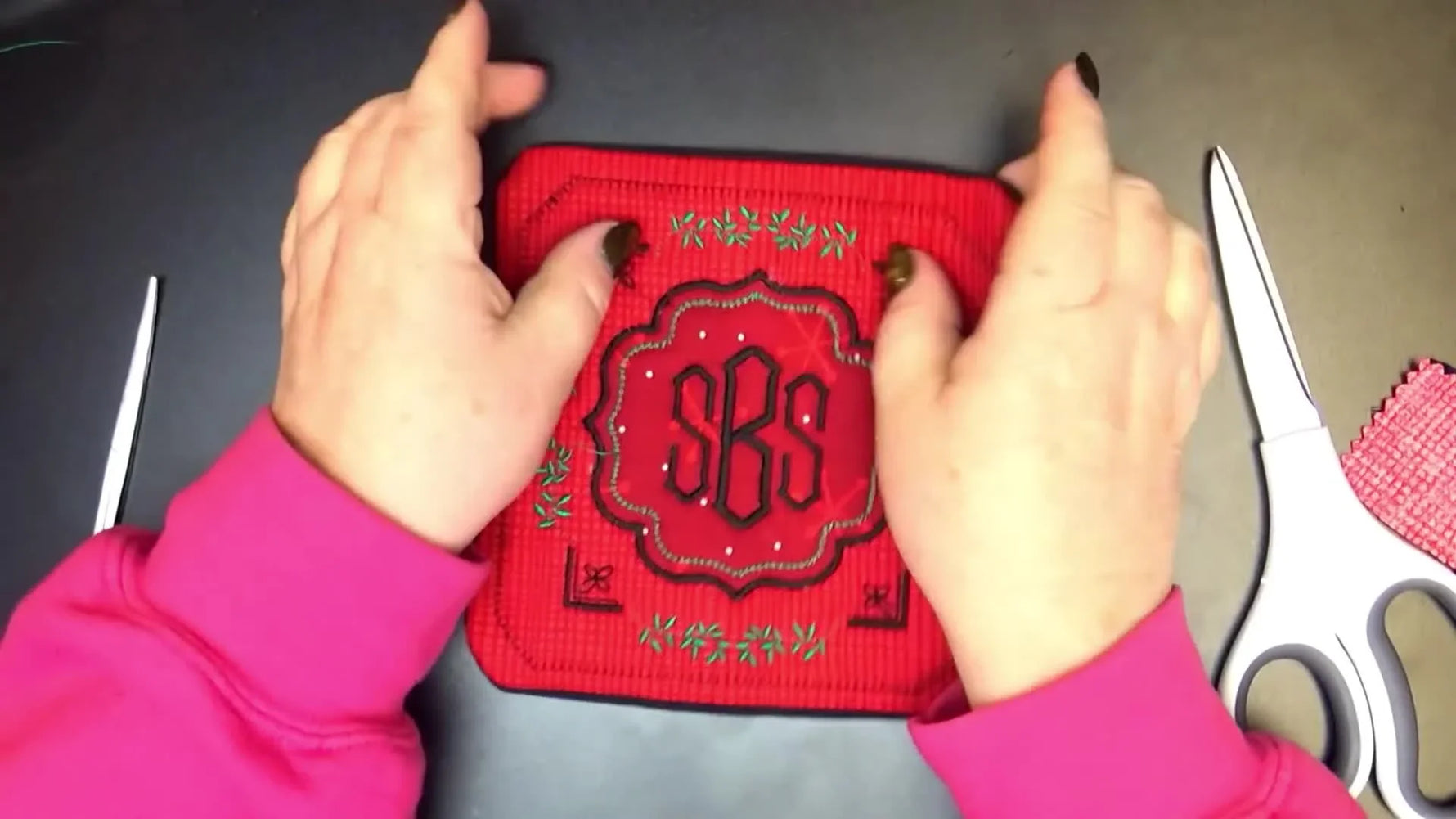A finished red-and-black in-the-hoop mug rug with decorative leaves, a bold satin appliqué border, and a centered monogram.