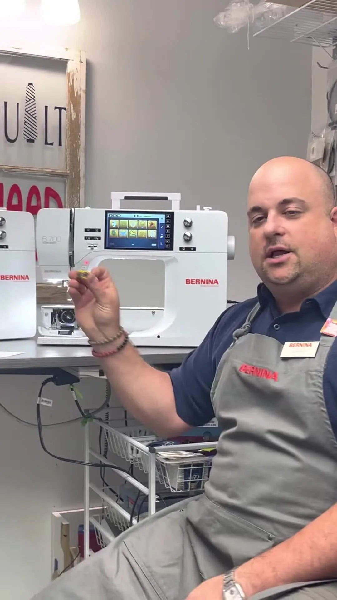 A close-up of the Bernina 700 yellow high-tension bobbin case held in hand, highlighting the key accessory that supports cleaner embroidery at higher speeds.