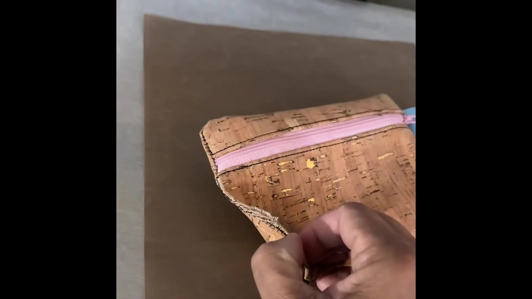 An overhead view of the finished cork ITH zipper pouch with a pink zipper and blue ribbon pull tab lying flat on a table.