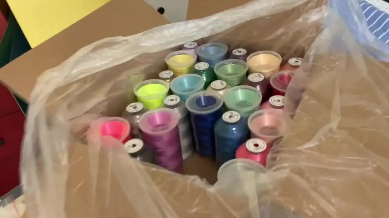 Overhead view of a large box packed with colorful 5000M embroidery thread cones from the 60-spool set.