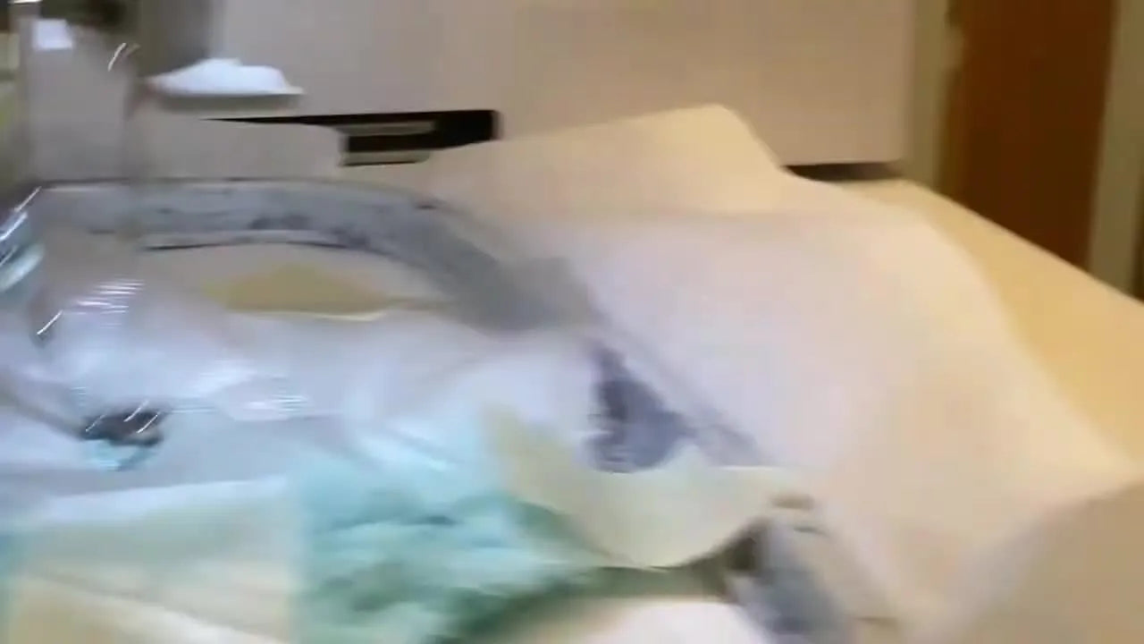 An extreme close-up of a Janome needle stitching teal satin letters into a plush bunny ear through a water-soluble topping.