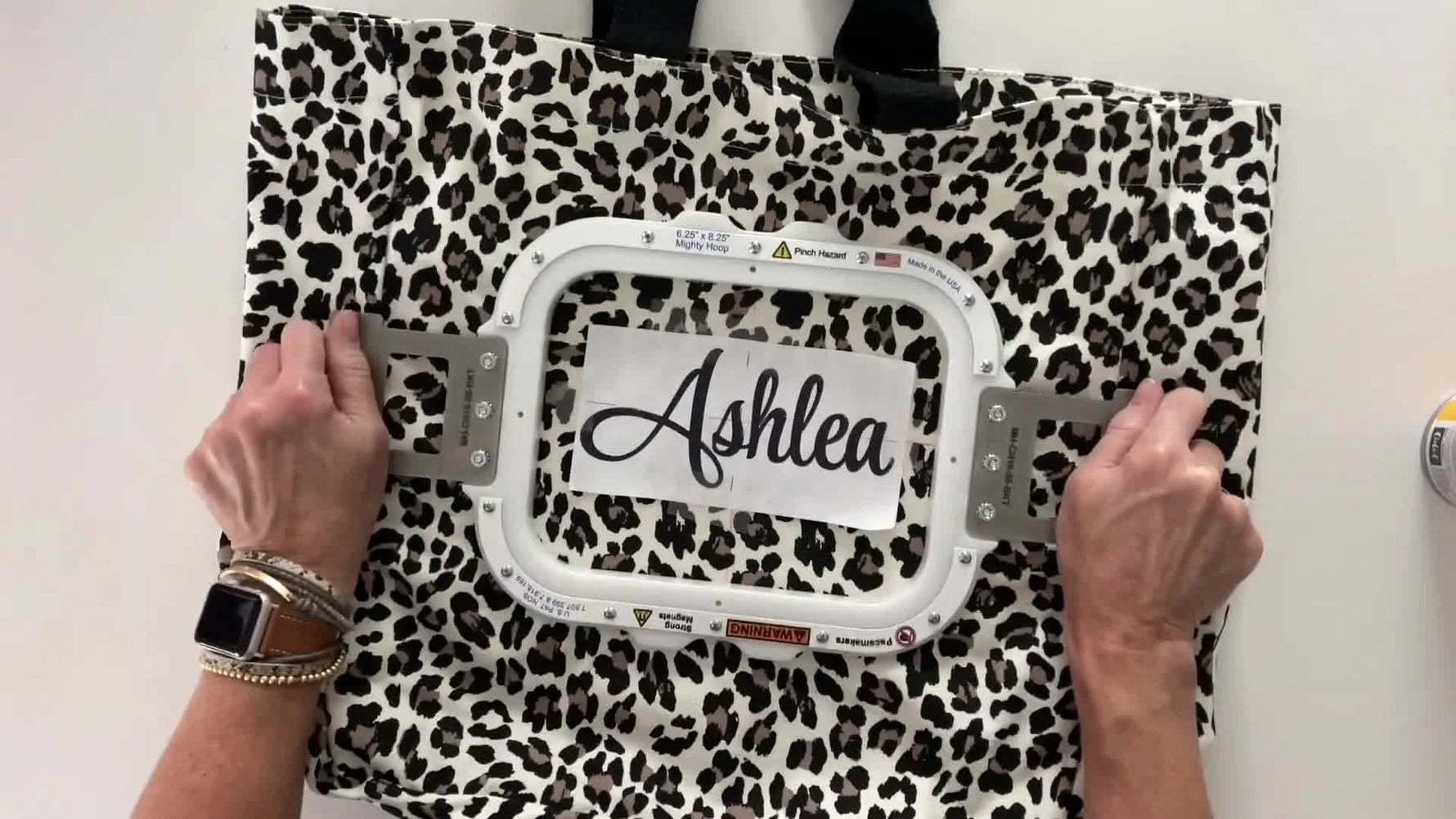 Hands snap a magnetic hoop closed on a leopard tote bag, instantly securing the fabric and stabilizer for embroidery.