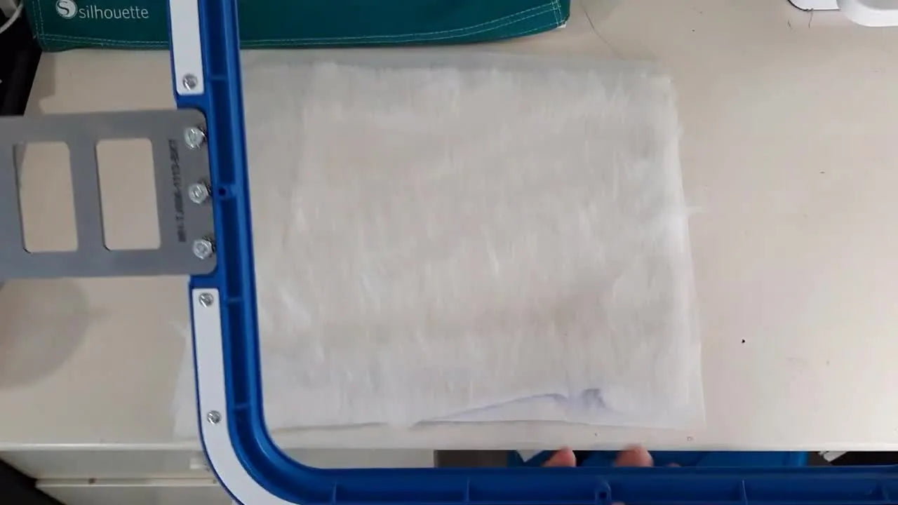 Hands drop the top blue magnetic frame onto high-pile faux fur and cutaway stabilizer to snap the hoop closed cleanly.