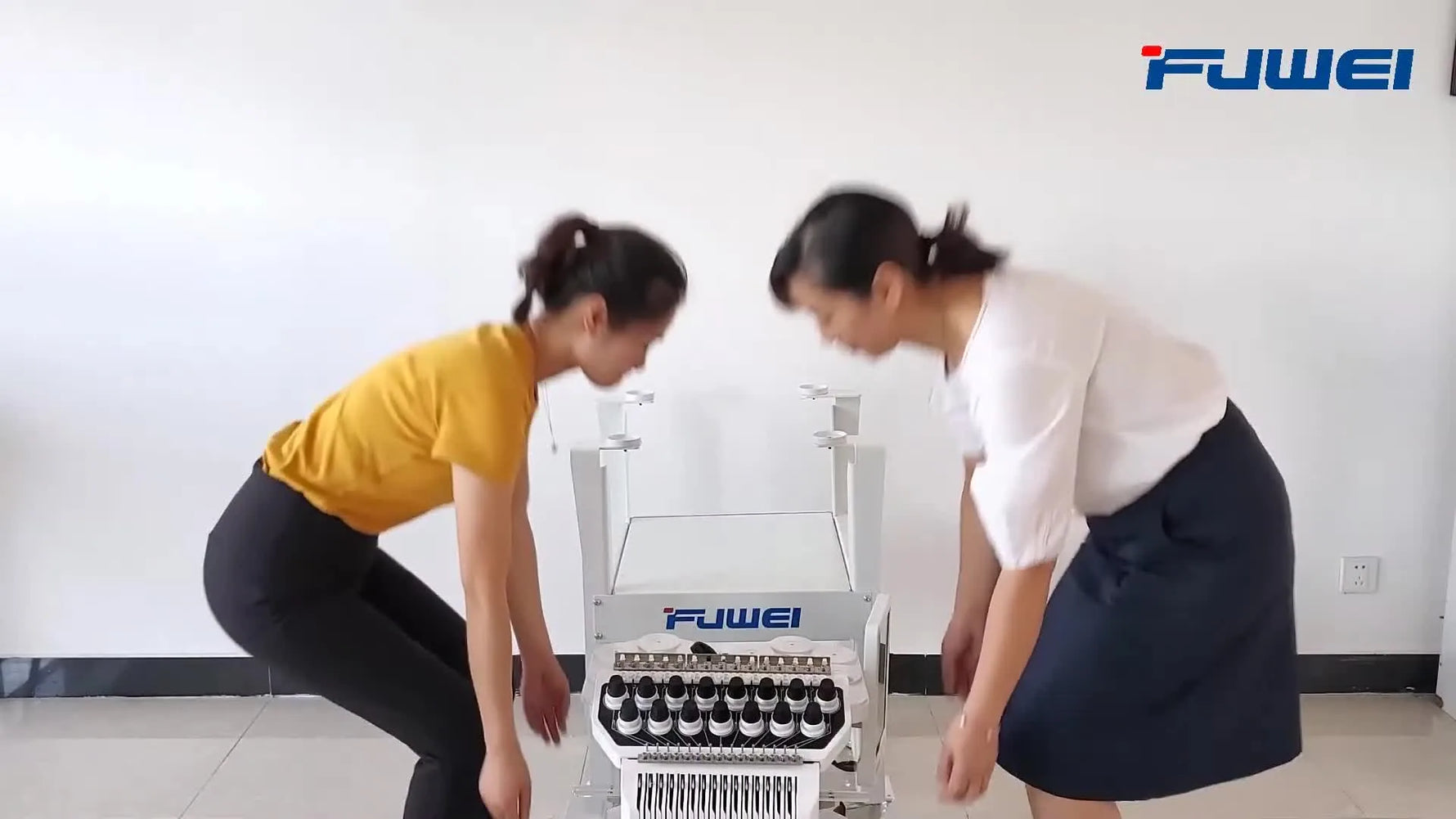 Two operators lift the FUWEI BF-1500 embroidery machine head from the crate and seat it onto the wheeled stand.