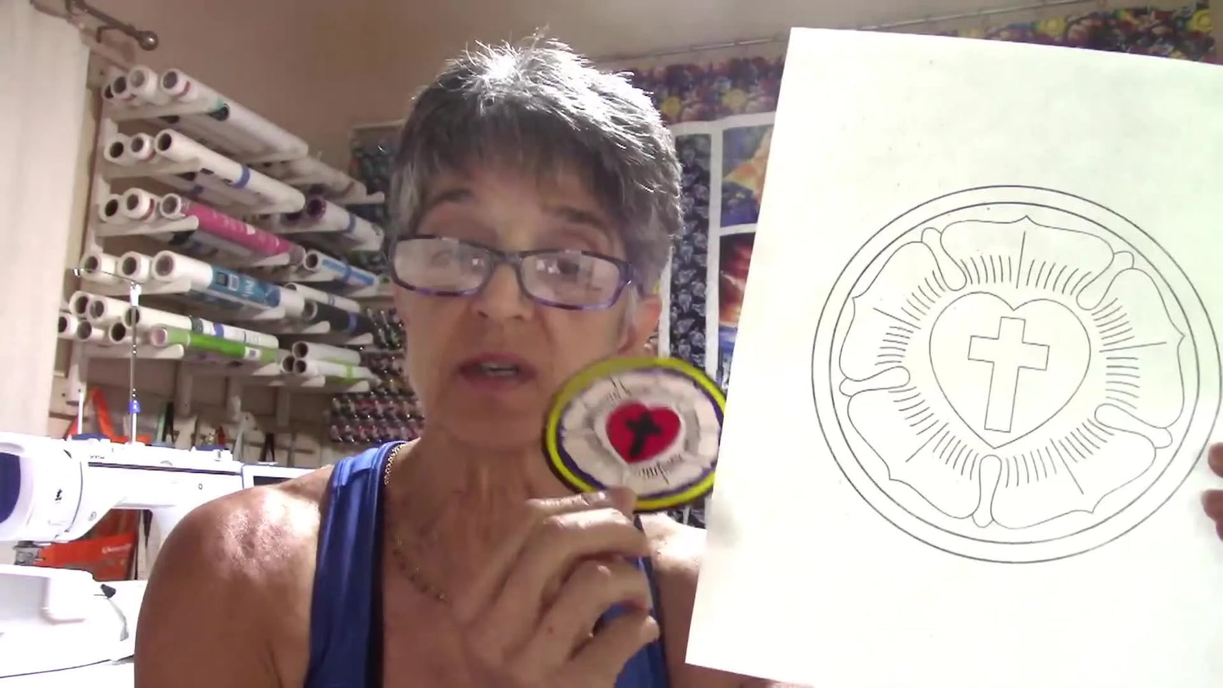 The presenter holds a paper line drawing beside the finished embroidered patch to show the “from sketch to stitch” transformation.