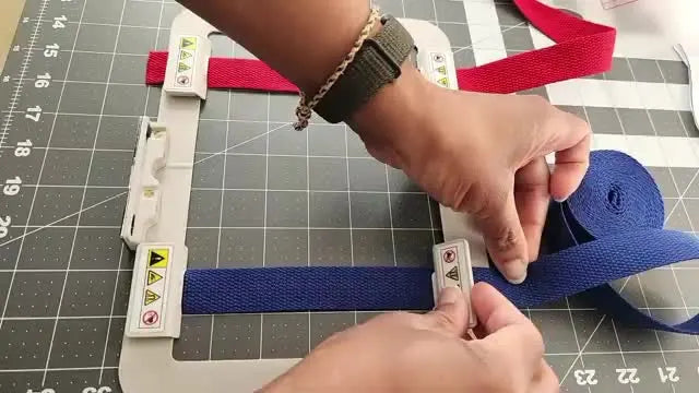 Overhead view of red and blue 1-inch webbing strips held perfectly parallel inside the SA444MK magnetic hoop using multiple rectangular magnets.