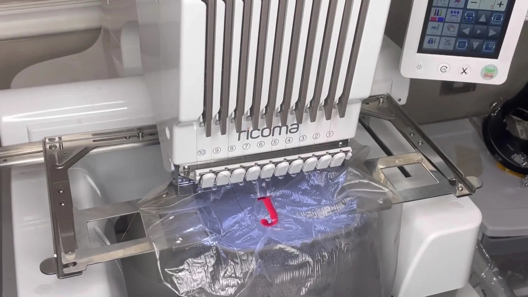 A Ricoma EM-1010 stitches a plush robe while clips hold bulky fabric away from the needle area.