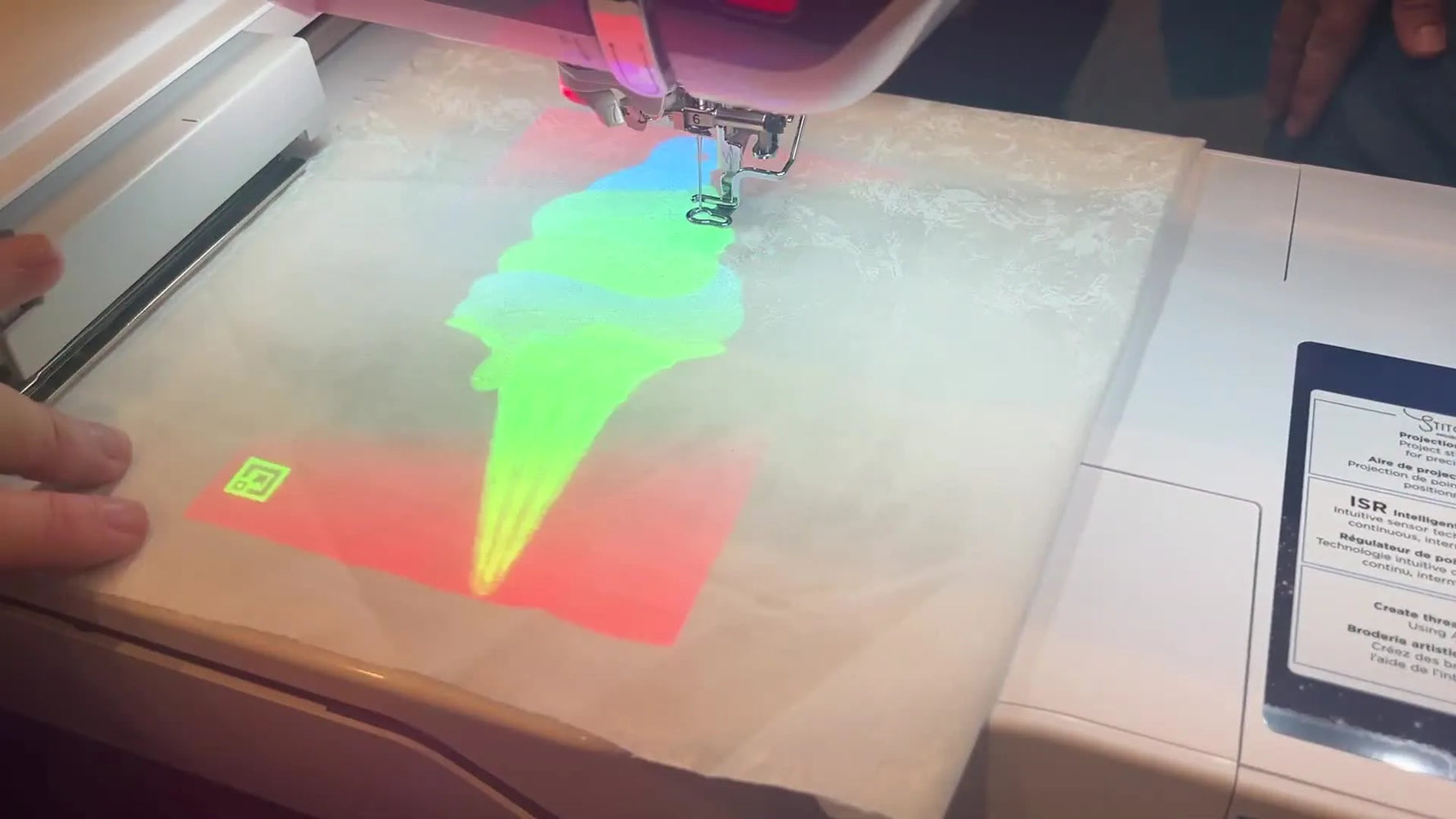 An ice cream cone embroidery design is projected in full color onto hooped fabric, showing exact placement before stitching.