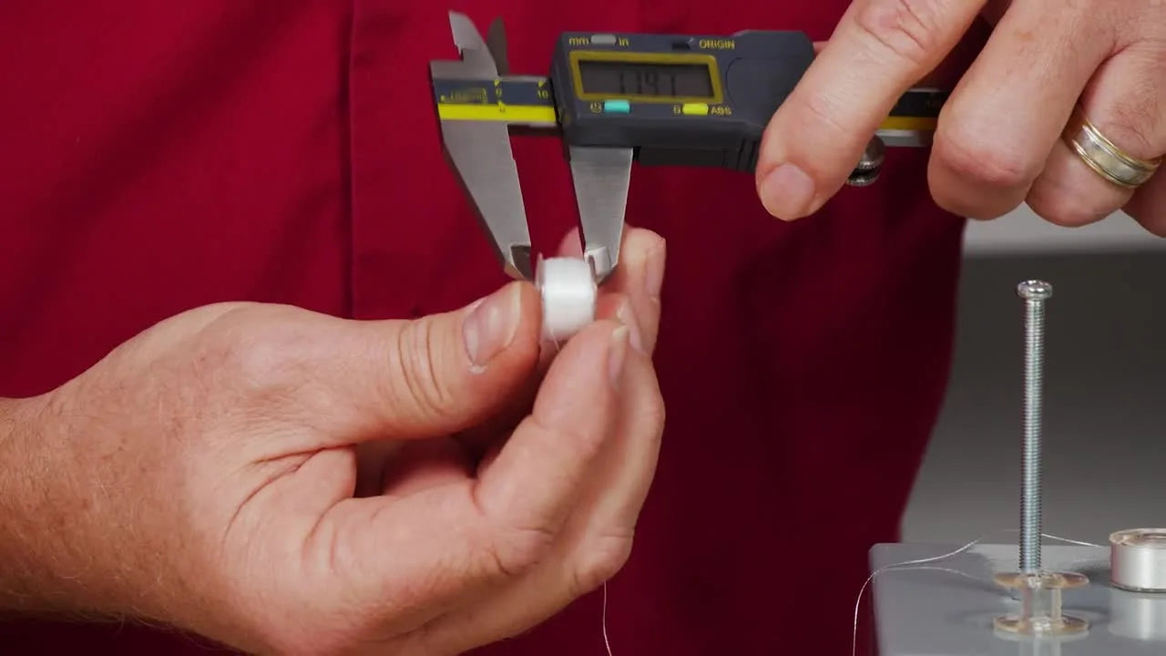 A close-up of a destroyed plastic bobbin with its top flange popped off and thread spilling out, illustrating what excessive winding tension can do.