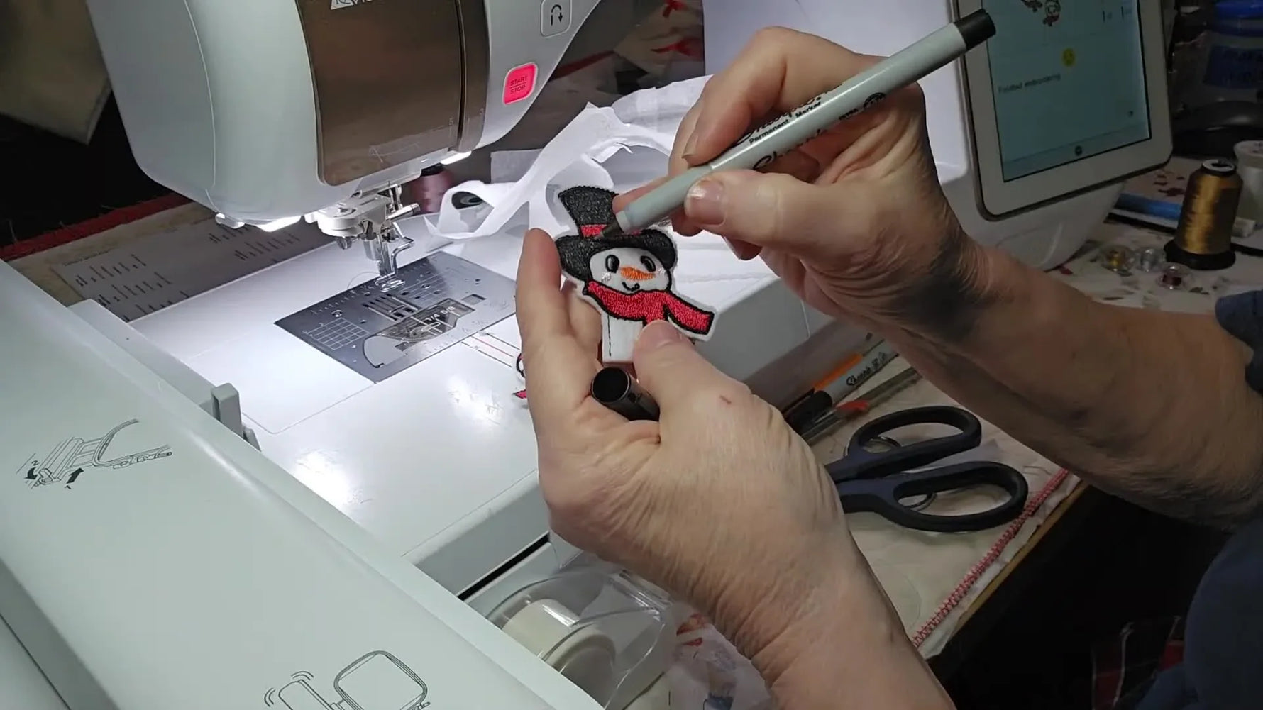 Two finished snowman and snowgirl ITH pencil toppers are held up side-by-side after trimming and final touch-ups.