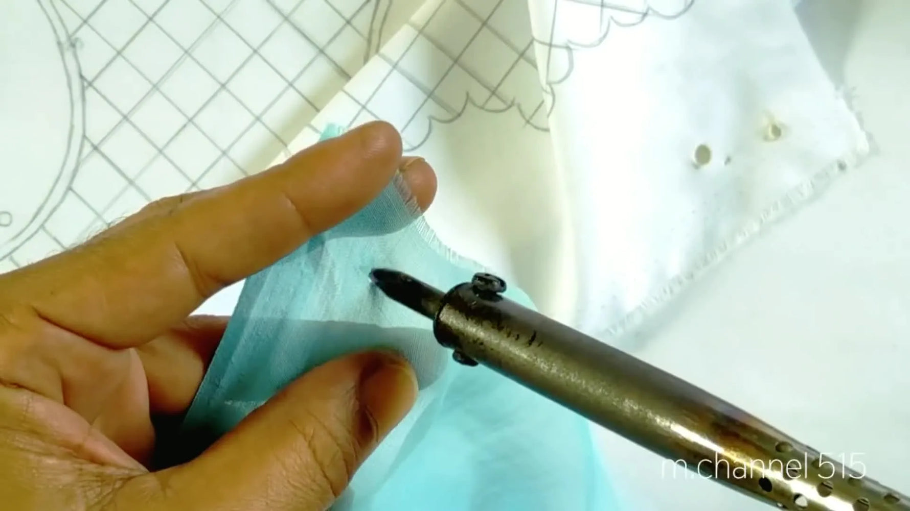 Close-up of a hand using a hot tool to melt small, circular holes in a light blue fabric.