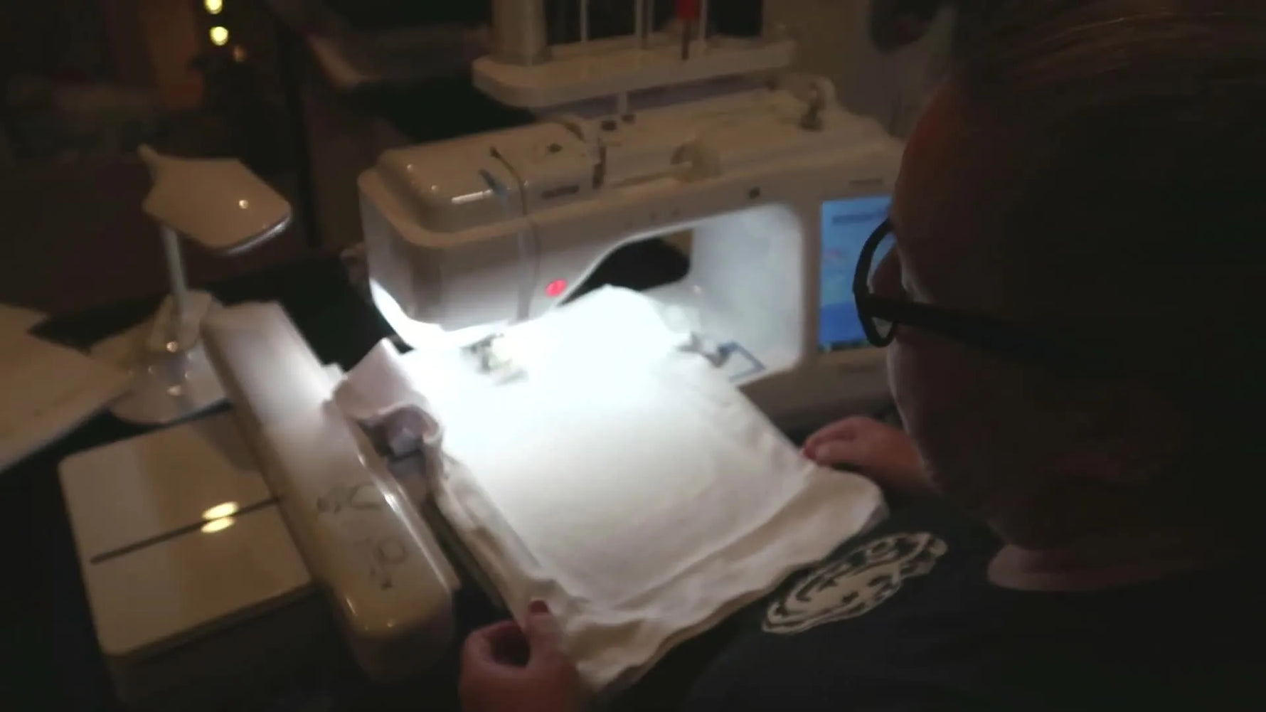 A white baby t-shirt attached to a hooped stabilizer being loaded into a Brother embroidery machine carriage.