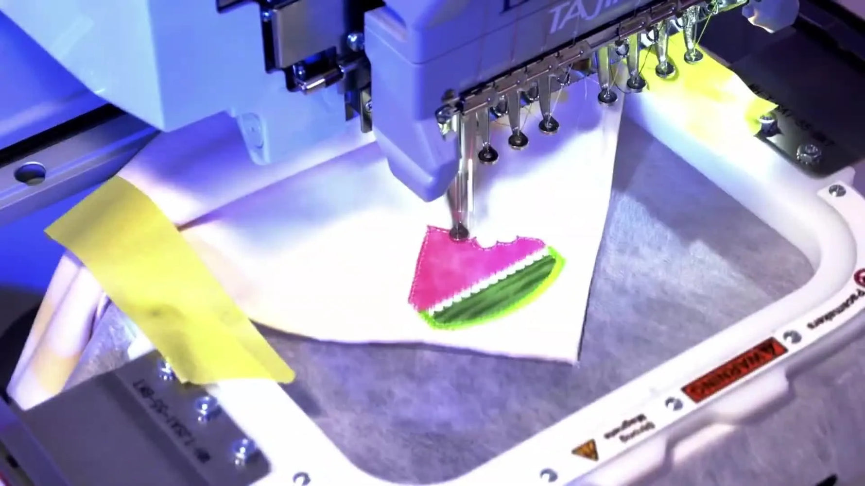 A close-up of the machine stitching the satin border and seeds as the watermelon napkin design reaches its final, polished stage.