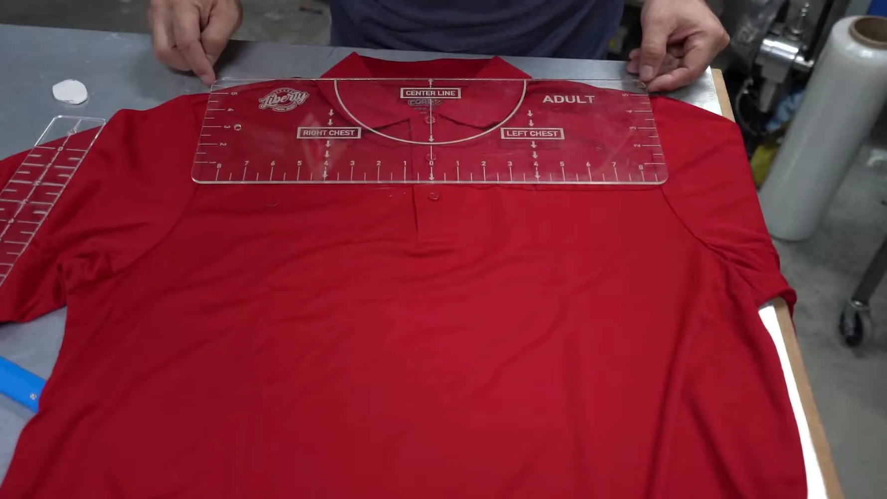 A close-up of the acrylic placement jig showing matching shoulder measurements (5.5 on both sides) to keep a left-chest logo perfectly level.