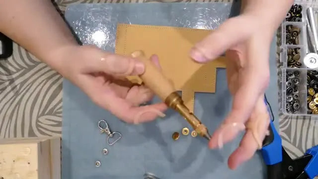 A close-up of a wooden-handled Japanese screw punch being held, ready to create clean holes for wallet hardware.