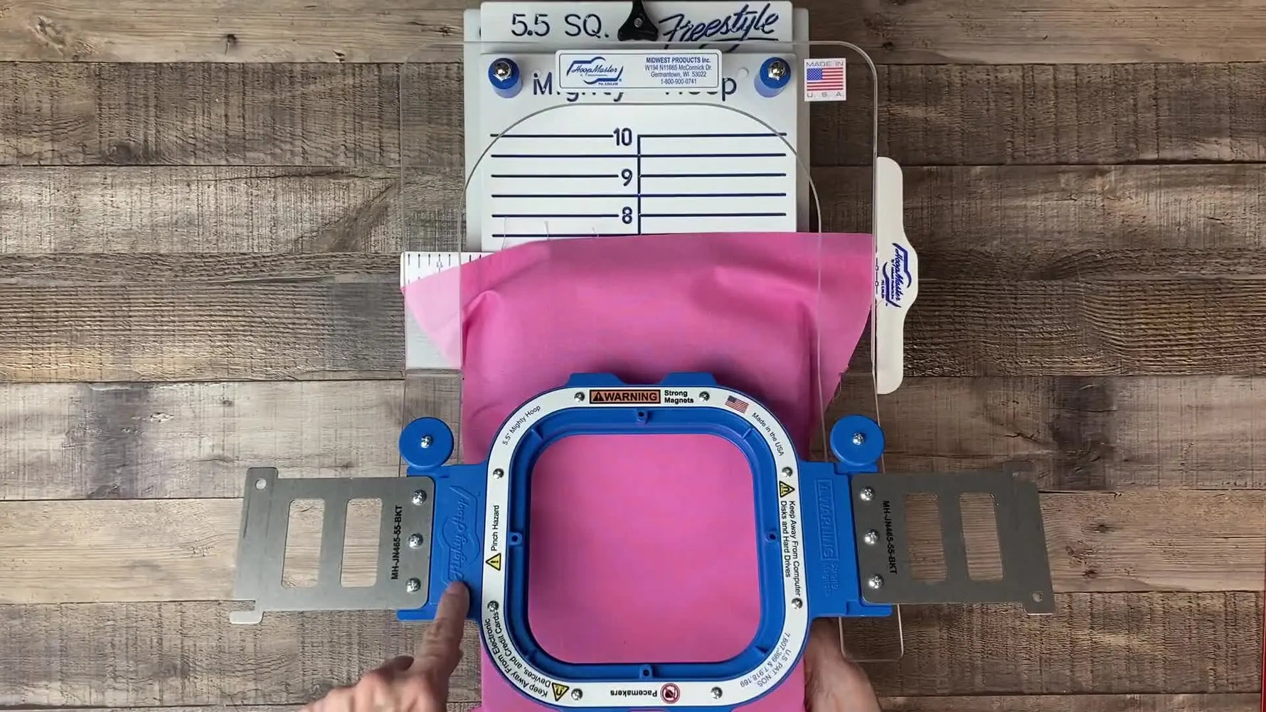 A 5.5-inch magnetic hoop is pressed down with one finger on a Freestyle Arm, showing how quickly the fabric clamps in place.