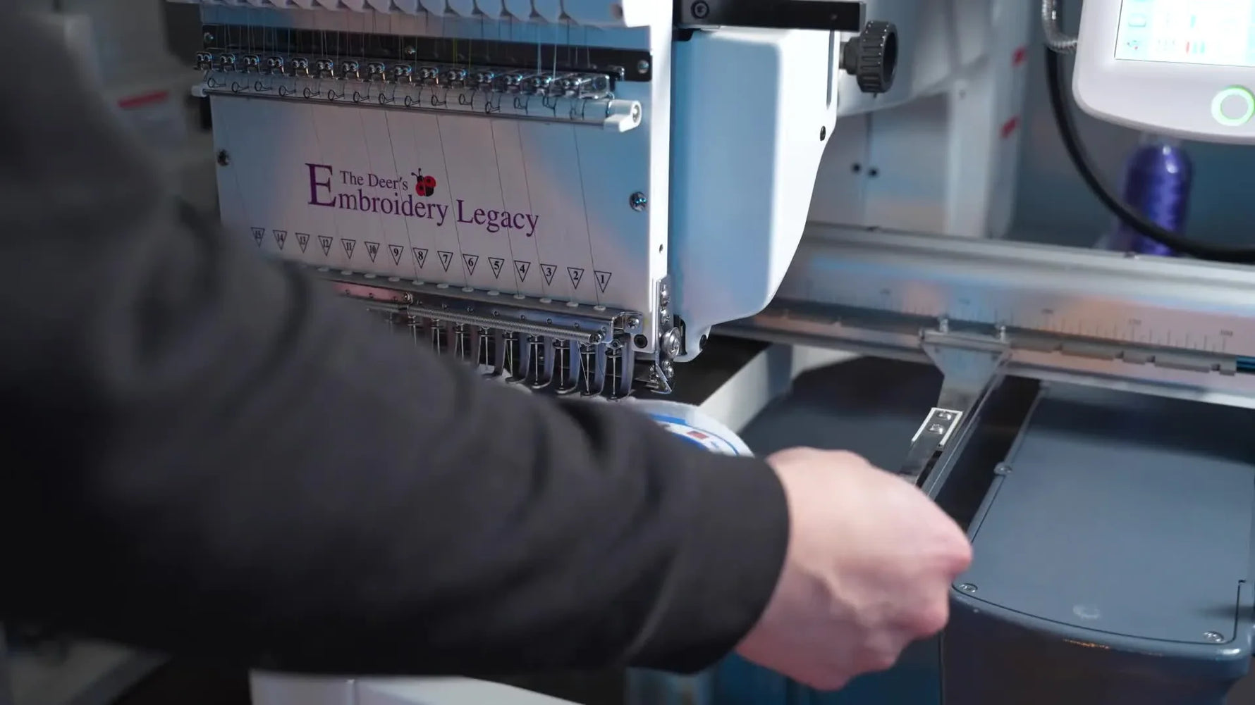 A close-up of a multi-needle embroidery machine stitching a rose outline on white felt held in a blue magnetic hoop.