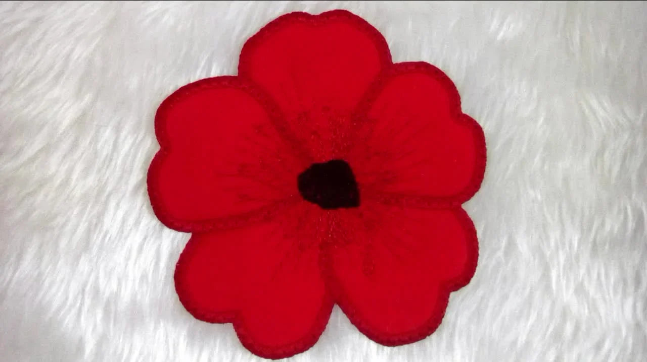 The finished red poppy coaster sits on a white fluffy background, showing a clean satin-stitched edge and crisp center details.