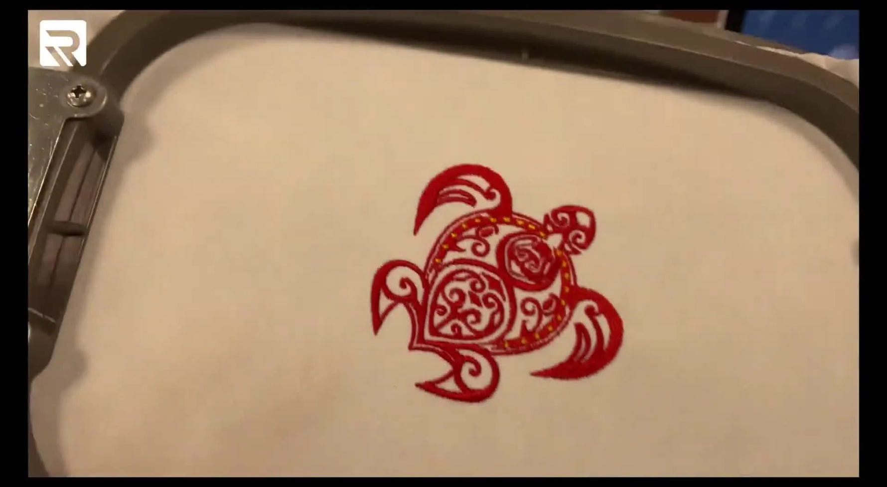 A finished red-and-yellow Tribal Turtle embroidery stitched on white fabric inside a hoop, shown close-up from above.