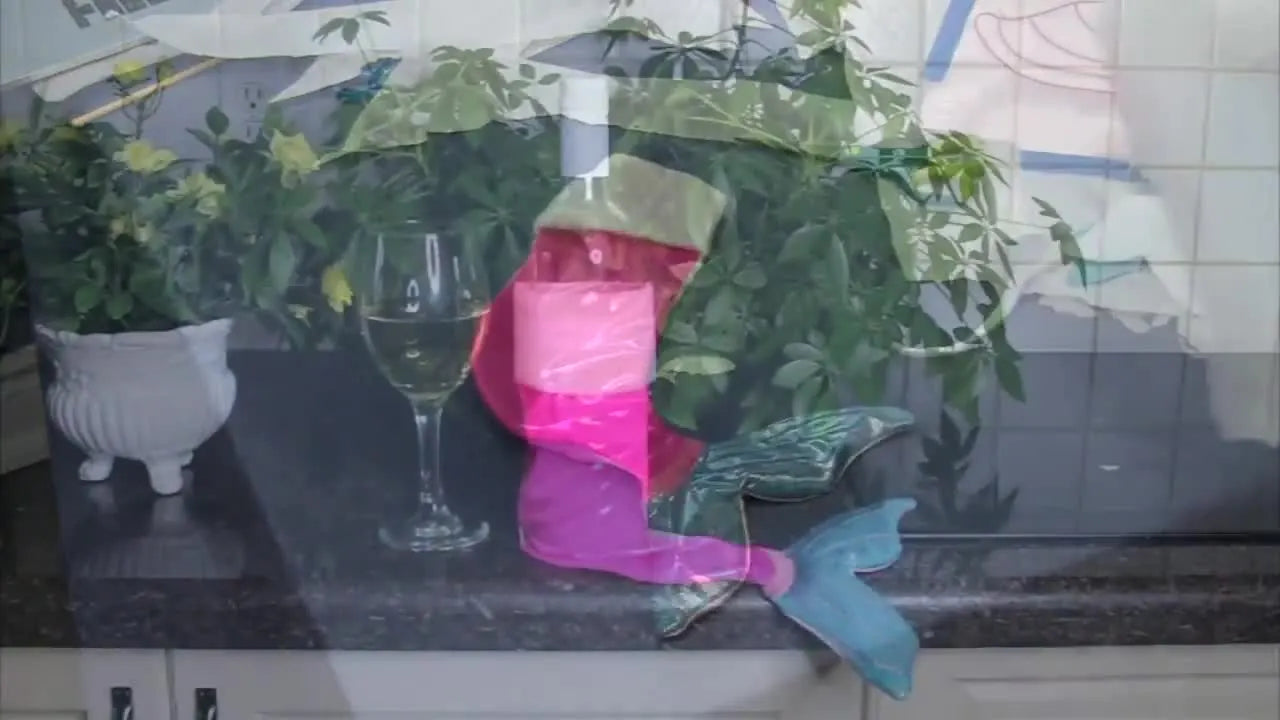 A finished mermaid-shaped ITH Christmas stocking is displayed on a counter beside a wine bottle, showing the sparkly body and tail with a clean joined seam.