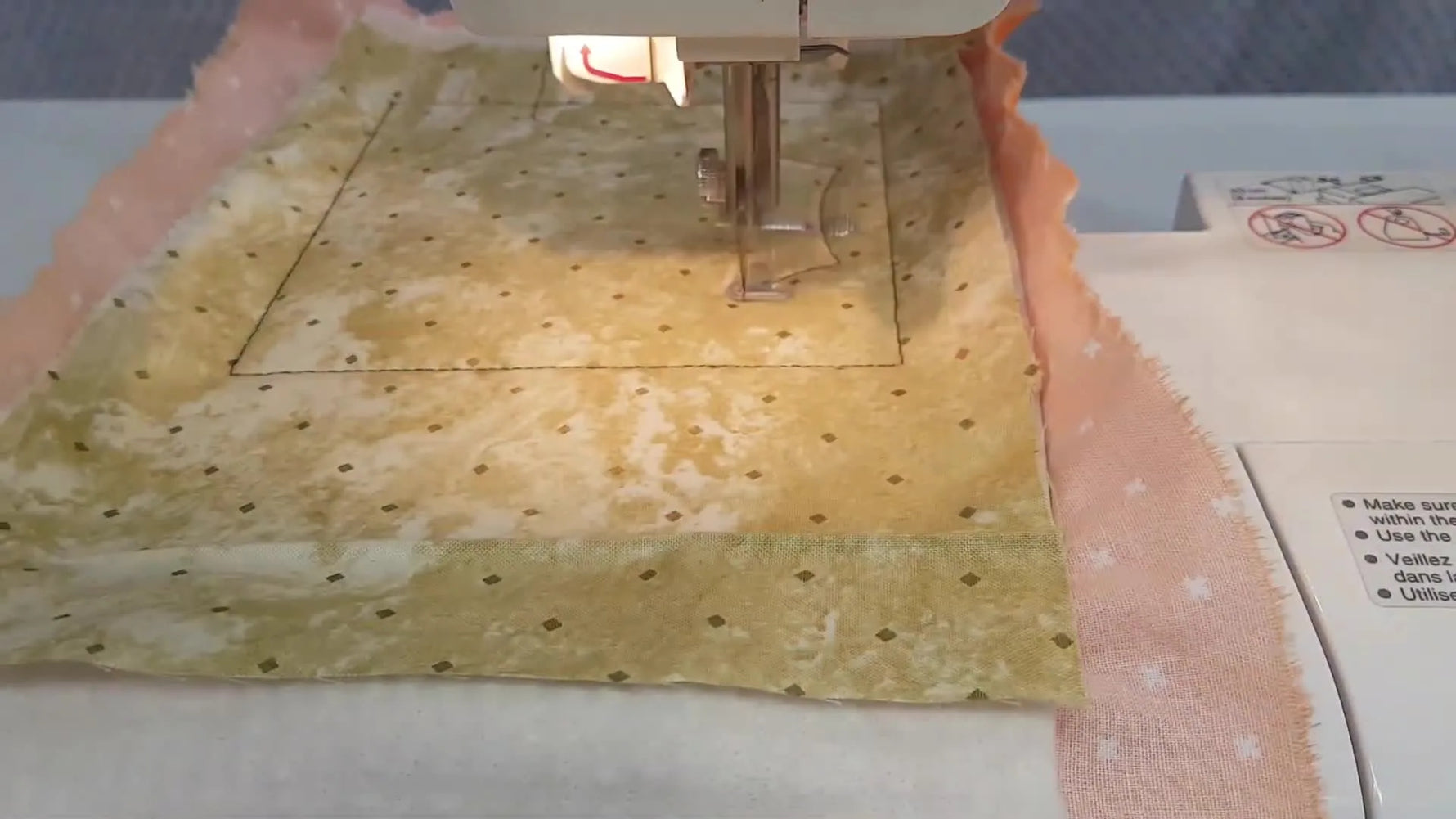 A close-up of the needle stitching curved spider web lines into a layered fabric sandwich inside the hoop.