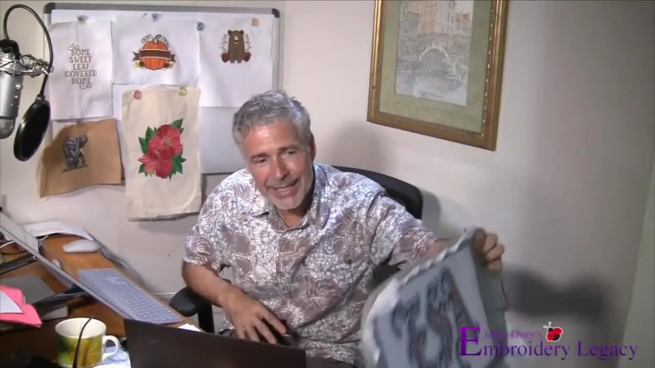 John holds a large rectangular hoop showing the gold-and-purple “ESA” Flexi Fill sample with a Mylar-style texture effect and satin borders.