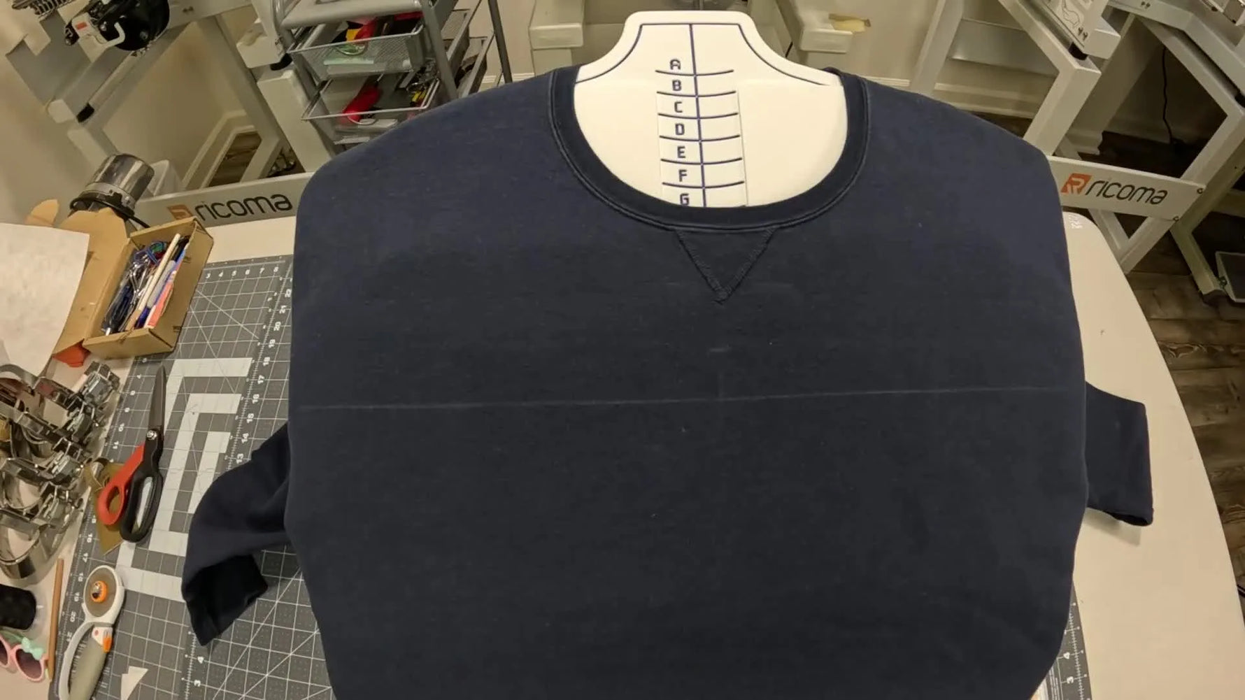 A top magnetic hoop frame is held above a hooped sweatshirt, ready to snap down for fast, even clamping.