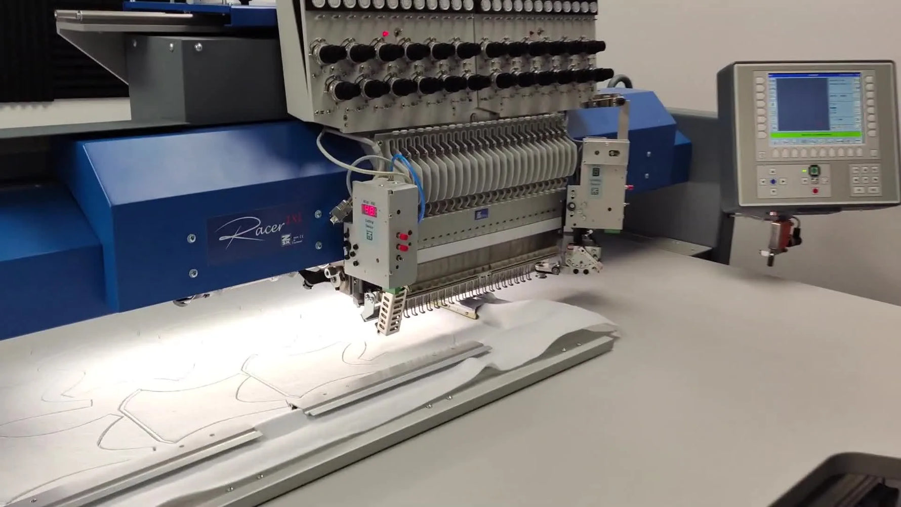 A close-up of a ZSK embroidery machine using a hot air cutter nozzle to cut mask shapes directly on the machine bed.