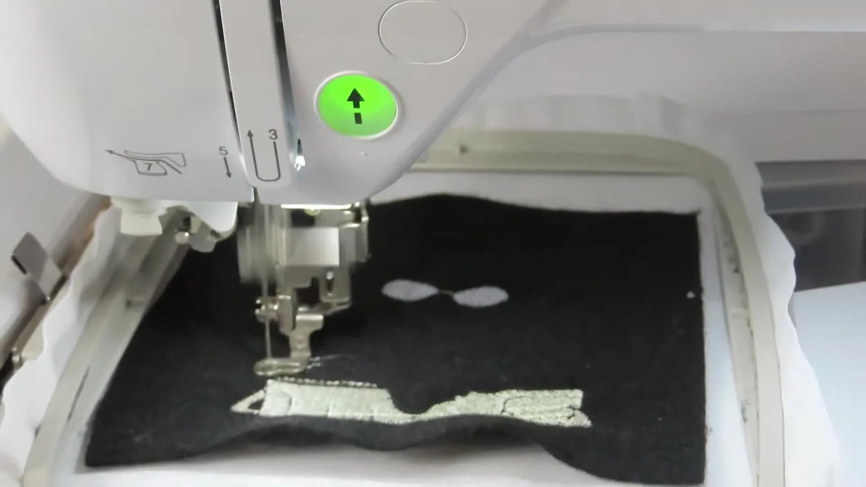 A nearly finished Oscar-style character patch sits cleanly in the hoop, showing crisp green and grey fills ready for the final black outline.