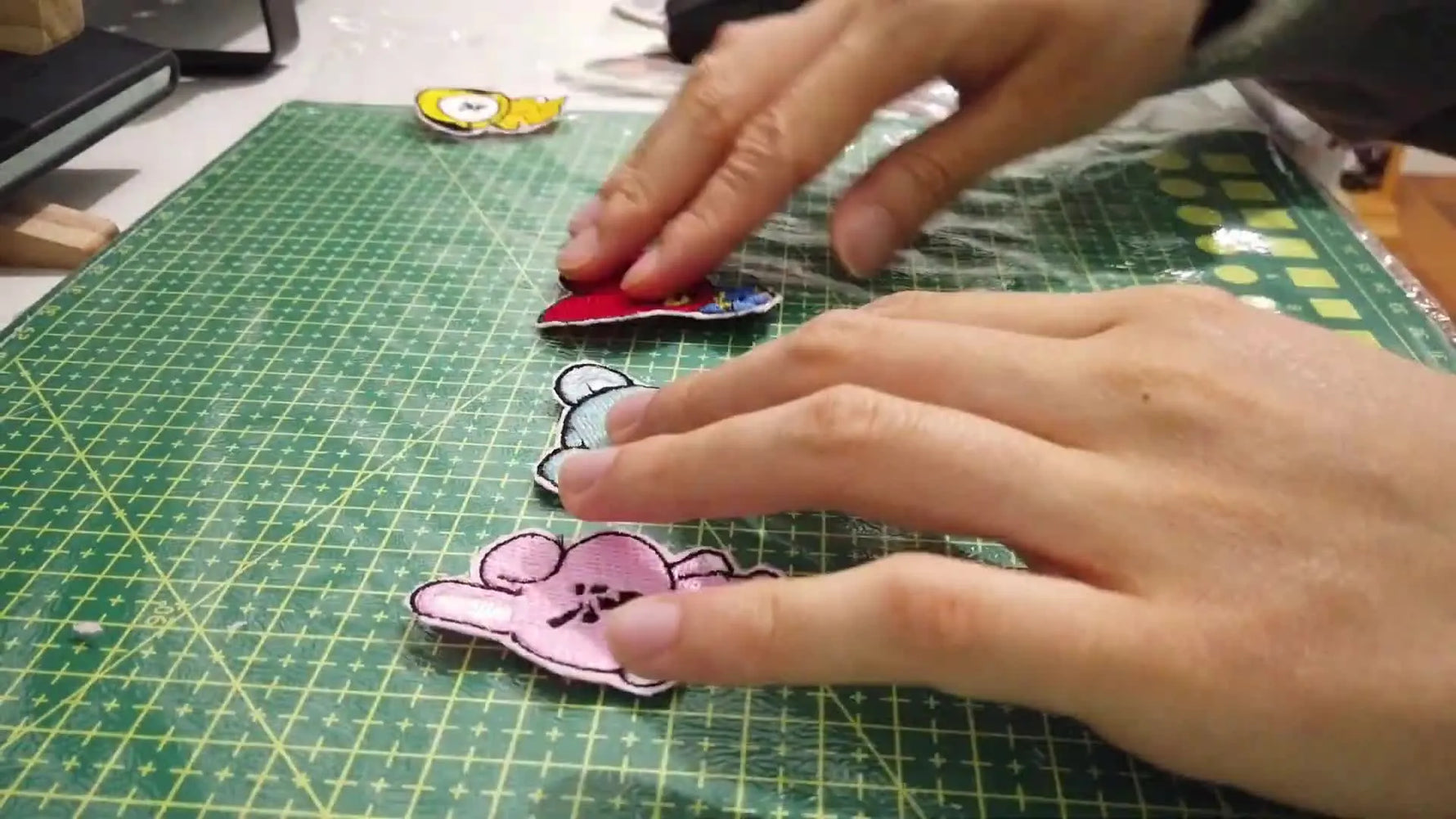 Four finished BT21-style embroidered patches are lined up neatly on a green cutting mat, showing clean borders and consistent stitch coverage.