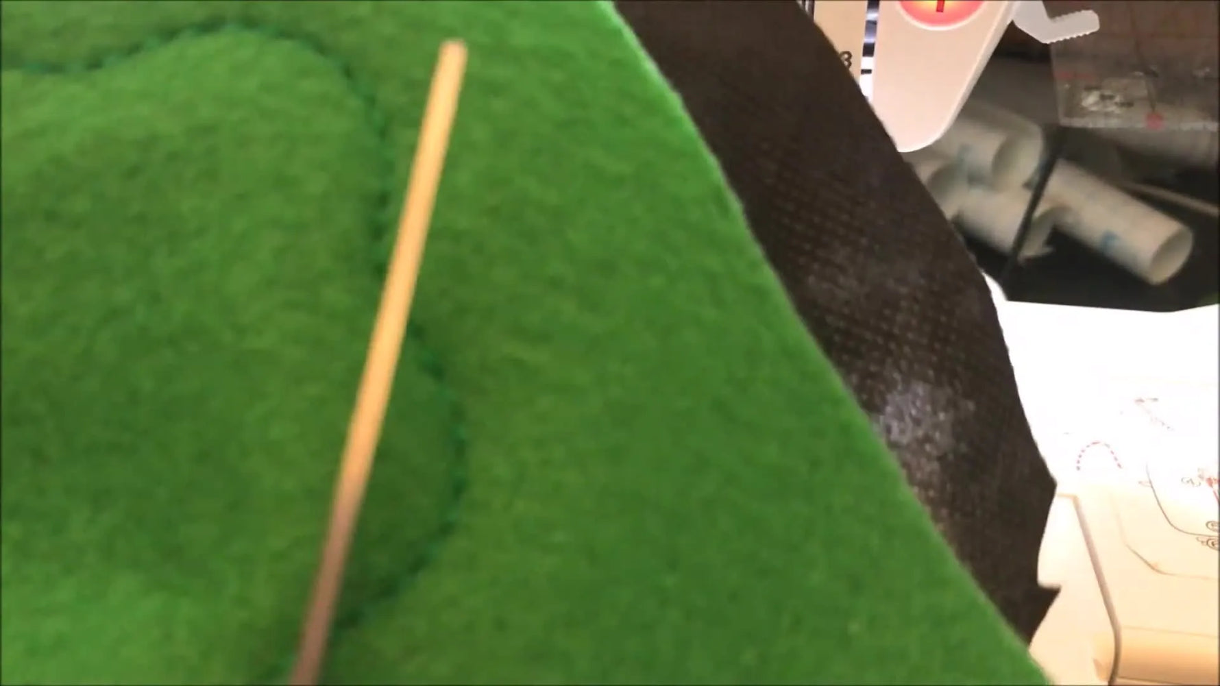 A finished green felt salad leaf is held up close, showing the stitched outline and clean cut edge.